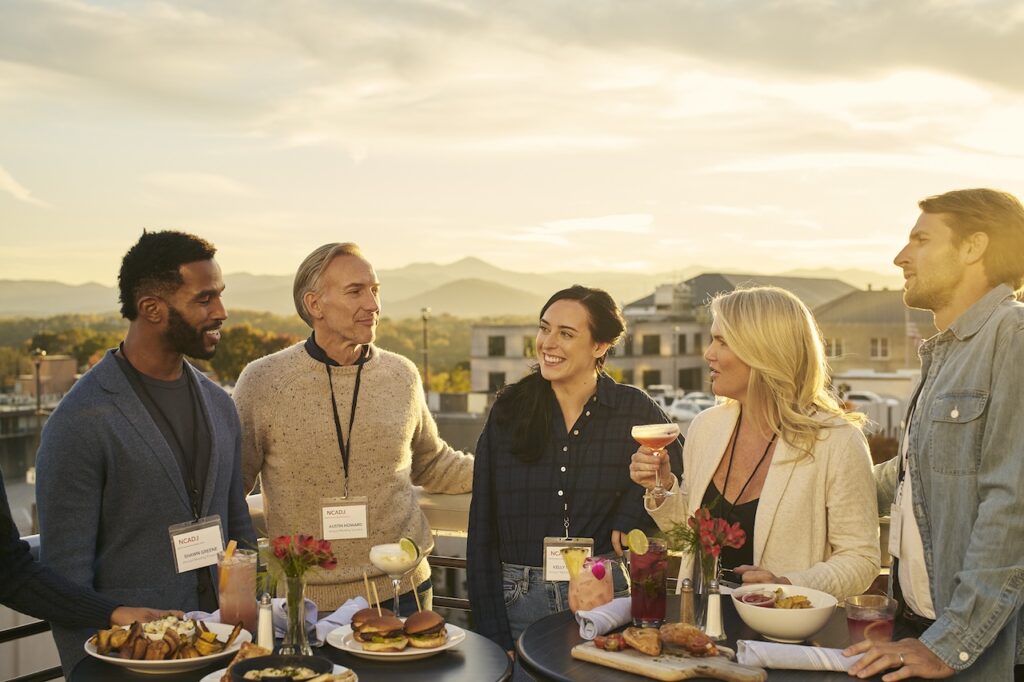 A group of people standing around a table with food and drinks.