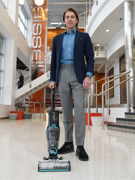 A man in a suit standing in a hallway with a vacuum.