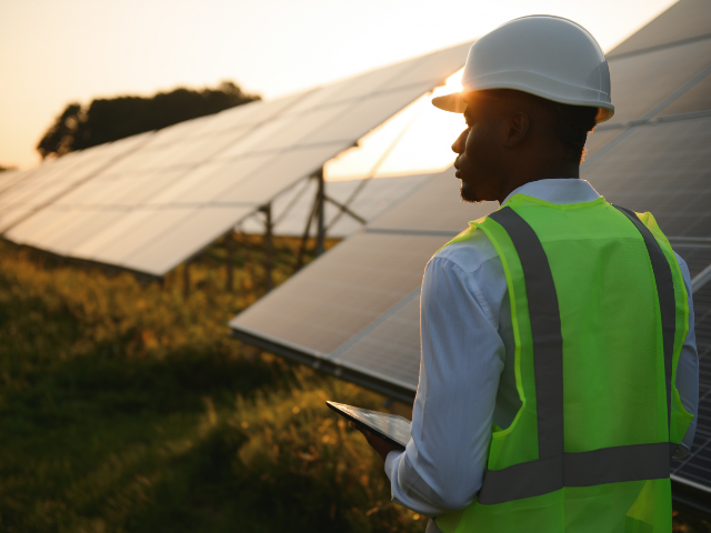A man wearing a hard hat is standing in front of solar panels.